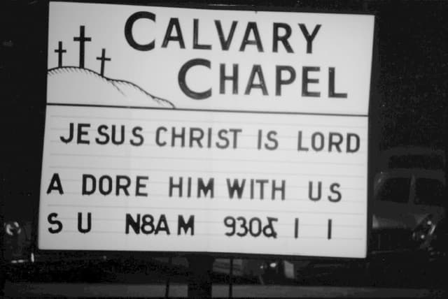 The Calvary Chapel sign at night: Jesus Christ is Lord. Adore Him with us. Black and white.
